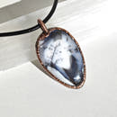 Colgante de merlinita —ópalo dendrítico— en bisel de cobre electroformado. Patrón de dendrites negras sobre fondo blanco y gris.