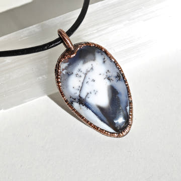 Colgante de merlinita —ópalo dendrítico— en bisel de cobre electroformado. Patrón de dendrites negras sobre fondo blanco y gris.