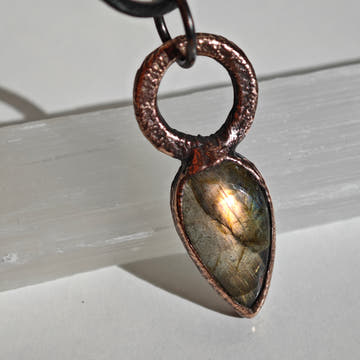 Colgante de labradorita lágrima en cobre electroformado con bail circular. Labradorescencia dorada y melocotón visible en el centro de la piedra.